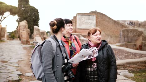 Young-Caucasian-female-excursion-tour-guide-giving-detail-on-historic-ruins-of-Ostia,-Italy-to-two-senior-women-tourists