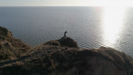 combative-sports-on-nature,-strong-boy-is-engaged-in-wrestling-on-hill-by-river-in-bright-sunshine-on-water-against-sky