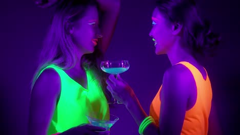 Langsame-Motin-von-schönen-sexy-Frauen-mit-fluoreszierenden-Make-up-und-Kleidung-Tanz-im-Neonlicht.-Night-Club,-Party-Konzept.