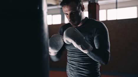 Ajuste-el-boxeador-entrenando-en-un-saco-de-boxeo-en-un-estudio-de-boxeo-interior
