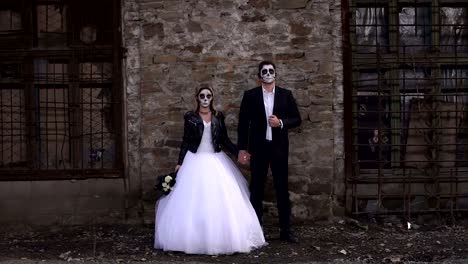 Creepy-couple-in-a-wedding-dress-with-makeup-for-Halloween-stand-near-brick-wall