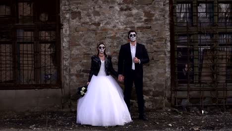 Gruselige-paar-in-ein-Hochzeitskleid-mit-Make-up-für-Halloween-Stand-in-der-Nähe-von-Mauer