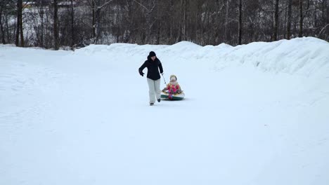 Frau-zieht-eine-Snow-Tube-mit-kleinen-Mädchen