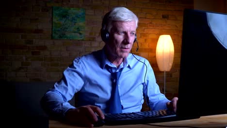 Closeup-portrait-of-old-caucasian-blogger-playing-video-games-on-the-computer-and-streaming-live-indoors-in-the-apartment-with-lights-off