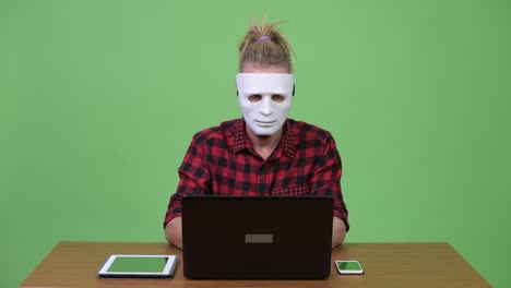 Hipster-man-wearing-mask-as-hacker-against-wooden-table