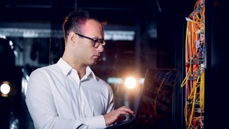 One-programmer-types-on-a-laptop-in-a-server-room,-close-up.