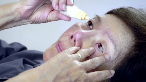 elderly-woman-tremor-applying-eye-drops-on-bed