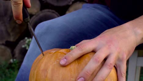 Man-carves-from-a-pumpkin-Jack-o'-lantern-in-the-backyard-on-a-tree-stump