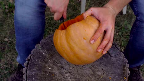 Man-carves-from-a-pumpkin-Jack-o'-lantern-in-the-backyard-on-a-tree-stump