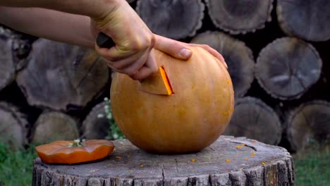 Man-carves-from-a-pumpkin-Jack-o'-lantern-in-the-backyard-on-a-tree-stump