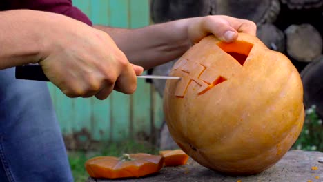 Man-carves-from-a-pumpkin-Jack-o'-lantern-in-the-backyard-on-a-tree-stump