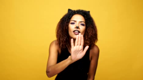 Happy-woman-cat-wearing-cat-ears-and-black-dress-wipe-glass-and-winking-isolated-over-yellow