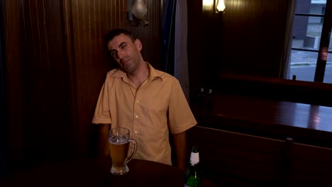 Drunk-guy-sitting-a-table-in-a-pub-cannot-hold-his-glass-with-beer