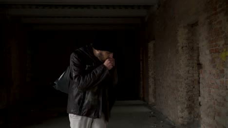 Sick-homeless-with-garbage-bag-walks-in-abandoned-building-in-search-of-food