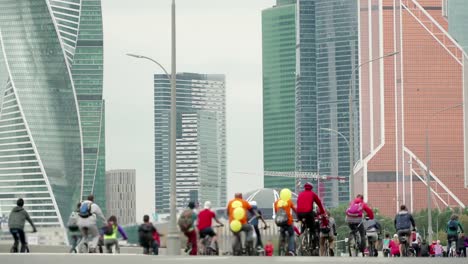 Bike-city-events-competition-in-background-of-skyscrapers,-crowd-of-cyclists-from-thousands-of-people-riding-bicycles,-unrecognizable-people-in-blur,-timelapse