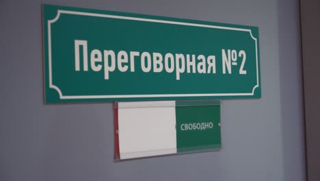 Mujer-se-mueve-la-placa-que-ocuparán-en-la-puerta-con-el-texto-ruso,-sala-de-reuniones