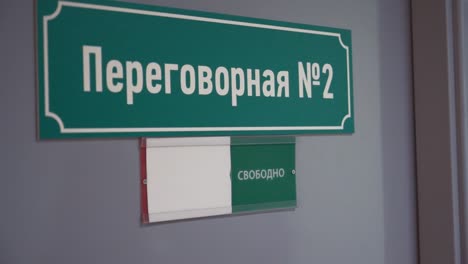 Woman-hand-moves-plate-to-occupied-on-door-with-cyrillic-text-meeting-room