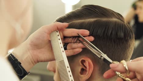 Woman-barber-combing-hair-and-cutting-with-professional-scissors-close-up.-Haircutter-doing-male-hairstyle-with-comb-and-hairdressing-scissors