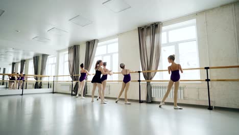 Delgado-chicas-aprenden-practicando-movimientos-de-ballet-en-amplio-estudio-luz-con-grandes-ventanas-y-barra-de-ballet-se-dobla-hacia-atrás.-Útil-tutor-es-enseñarles.