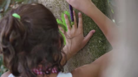 Happy-young-girl-in-summer-camp-making-marks-with-hands-and-paint-on-trees-art-outside-kids-playing-outdoor-in-park-under-trees-slow-motion