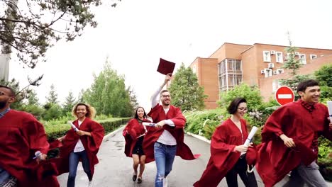 Slow-Motion-der-Frohe-Absolventen-laufen,-hält-Diplome-und-winken-Mortarboards-Freiheit-zu-genießen.-Höhere-Bildung,-Jugend-und-Glück-Konzept.