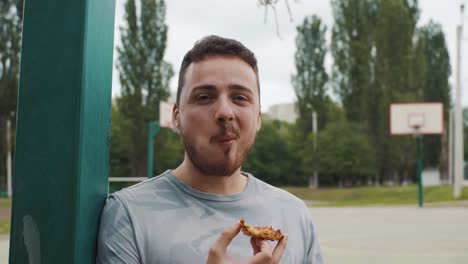 Nahaufnahme-eines-gutaussehenden-Mann-Essen-Pizza-auf-einem-Basketballfeld