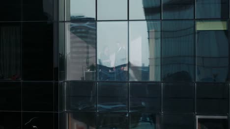 Aerial-Footage-From-Outside-of-the-Skyscraper:--Businessman-and-Businesswoman-Talking-Business-while-Standing-in-the-Office-Window.-Flying-Shot-of-the-Financial-Business-District-and-Businesspeople-Working-in-the-Big-City.