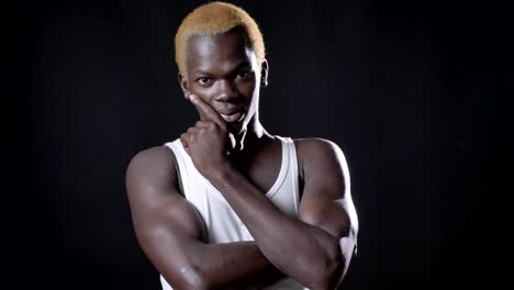 Young-thoughtful-blond-african-american-man-in-white-shirt-standing-and-holding-his-face,-isolated-on-black-background