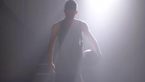 Basketball-player-doing-different-tricks-with-ball,-spinning-and-waving,-standing-in-dark-gym-with-fog