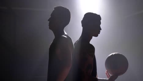 Zwei-Basketball-Spieler-Silhouette-stehen-Rücken-an-Rücken-in-Raum-mit-Rauch-und-Flutlicht