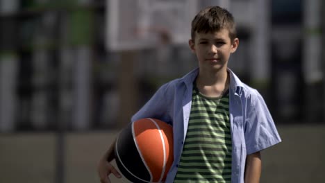 Retrato-de-un-niño-con-una-pelota-de-baloncesto-en-una-cancha-de-baloncesto,-mira-a-la-cámara