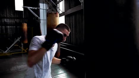 Boxer-hombre-caucásico-en-camiseta-y-camisas-rojas-ejercitándose-en-el-gimnasio.-Practicando-patadas-y-puches-con-saco-de-boxeo.-Boxeo-en-el-interior-del-estudio