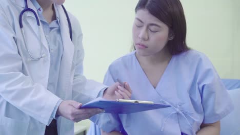 Beautiful-smart-Asian-doctor-and-patient-discussing-and-explaining-something-with-clipboard-in-doctor-hands-while-staying-on-Patient's-bed-at-hospital.-Medicine-and-health-care-concept.