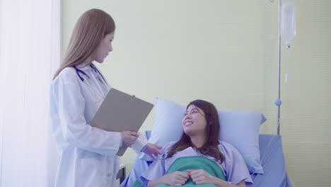 Beautiful-smart-Asian-doctor-and-patient-discussing-and-explaining-something-with-clipboard-in-doctor-hands-while-staying-on-Patient's-bed-at-hospital.-Medicine-and-health-care-concept.