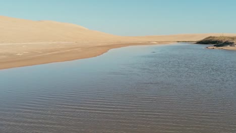 aerial-footage-of-a-beautiful-blue-lagoon-next-to-the-desert-sand-dunes-with-a-football-gate-in-the-water