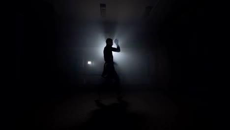 Sportsman-boxing-in-smoky-studio.-Silhouette-on-dark-background.-Boxer-training