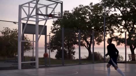 Handhelded-footage-of-young-girl-in-shorts-and-white-golf-socks-make-a-shot-to-the-basketball-net.-Outdoors,-trees-on-the-background