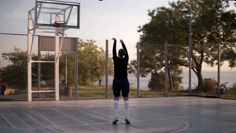 Chica-joven-en-prácticas-de-ropa-deportiva-lanzando-una-bola-en-el-aro.-Jugador-de-baloncesto-profesional-ejercer-en-la-corte-por-la-mañana.-Raro-ver