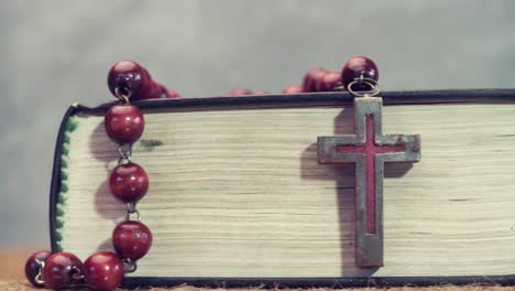 Open-Bible-and-the-crucifix-beads-on-a-golden-table,-close-up.-Beautiful-dark-background.-Religion-concept