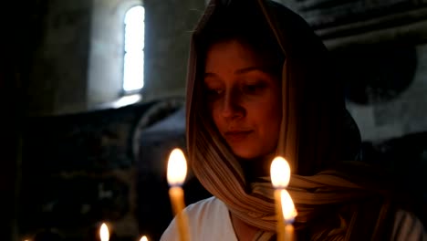 Woman-in-a-headscarf-puts-a-candle-and-prays-before-the-icon-in-the-Orthodox-Catholic-Church