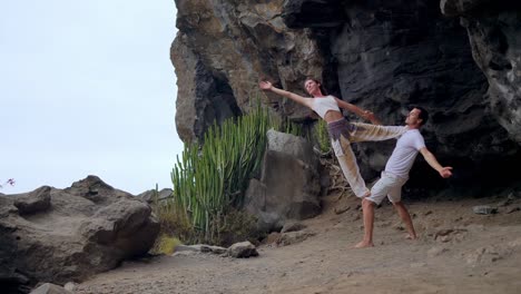 Ein-Mann-und-eine-Frau-stehen-am-Rand-einer-Klippe-mit-Blick-auf-den-Ozean-erheben-ihre-Hände-oben-und-atmen-Sie-die-frische-Seeluft-während-yoga