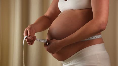 Pregnant-woman-checks-her-belly-with-tape-measure