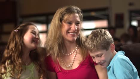 A-woman-hugs-and-kisses-a-young-girl-and-boy-while-reading-a-book-inside