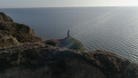 artes-marciales-en-bello-paisaje,-deportista-comprometido-Kickboxing-en-colina-por-el-mar-en-luz-del-sol-sobre-el-agua-contra-el-cielo