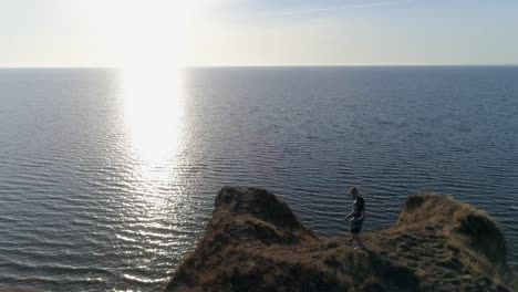 deportes-al-aire-libre,-atleta-en-ropa-deportiva-entra-en-pendiente-al-agua-de-mar-en-la-naturaleza-en-la-montaña-contra-el-cielo-en-luz-solar-brillante