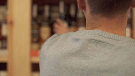 Man-takes-and-puts-back-wine-bottle-closeup-Customer-is-choosing-drink-in-alcohol-shop