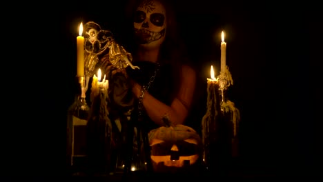 Halloween-Hexe-mit-Schädel-Make-up-macht-Voodoo-hält-Messer-und-wispering-Zauber-magische-Kürbisketten-und-Kerzen