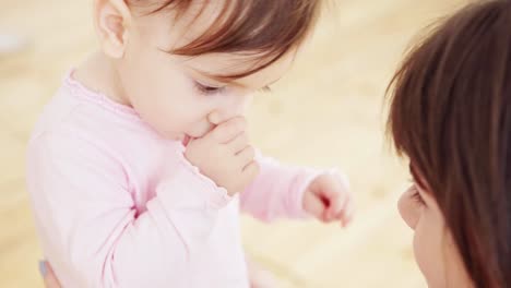 Cerca-de-una-joven-madre-amorosa-jugando-con-su-linda-niña-con-grandes-ojos-marrones-chupando-su-pulgar