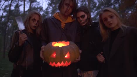 Alto-hombre-guapo-sosteniendo-calabaza-de-Halloween-con-una-luz-en-el-interior-de-cerca,-tres-chicas-bonitas-de-pie-cerca