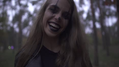 Crazy-young-woman-with-Halloween-clown-makeup-on-her-face-holding-big-knife-in-hand,-laughing.